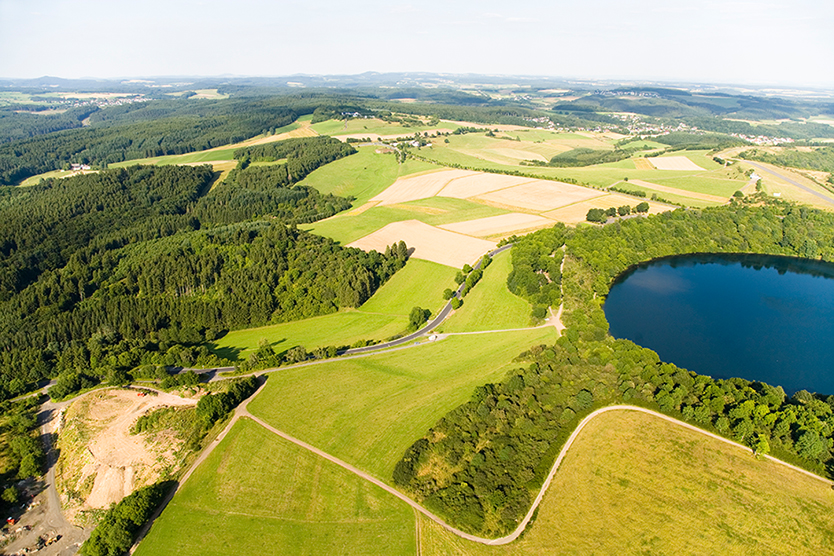 Luftaufnahme einer Landschaft mit Wald und See zu Klimaschutz.
