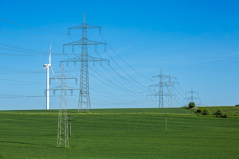 Strommasten und Windrad stehen für Energieversorgungssicherheit.