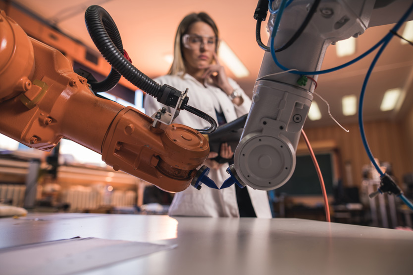 Automatisierte Roboterarme im Labor mit einem Ingenieur im Hintergrund