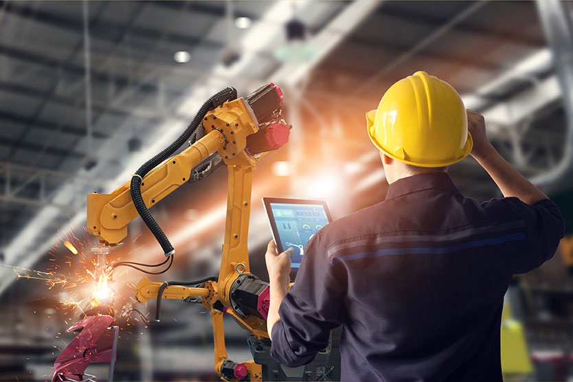 Ingenieur mit Tablet prüft Roboter, symbolisiert Industrie 4.0