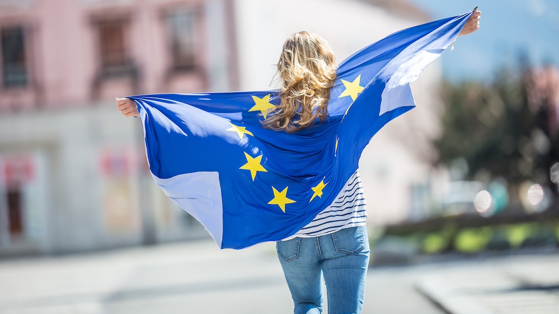 Junger Mensch mit der im Wind flatternden Flagge der Europäischen Union auf dem Rücken.