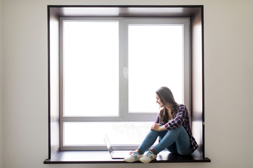 A woman is sitting at a window holding a laptop – symbol for the Digital Agenda