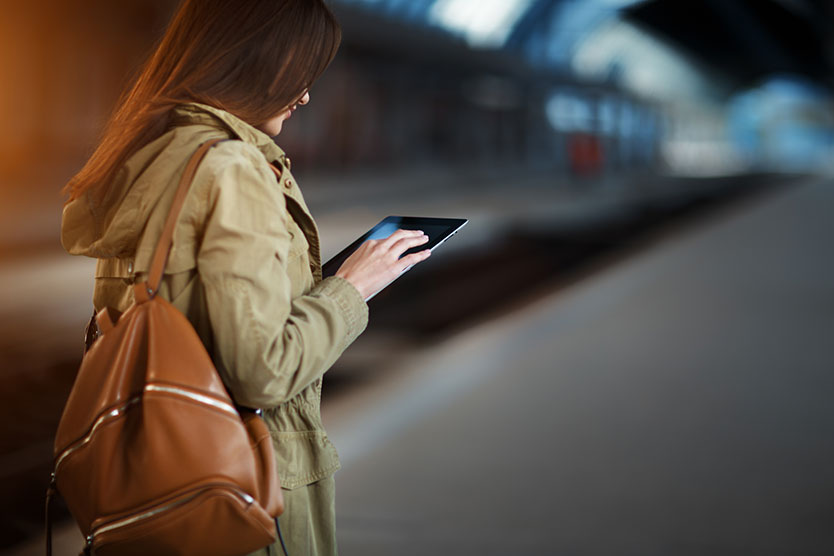 Young woman with backpack using tablet while standing on the railway station platform