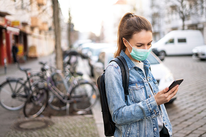 Young woman wearing protective mask looks at her smartphone