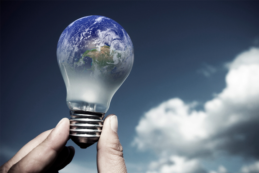 Hand holding light bulb containing image of the Earth against the sky, representative of international energy policy
